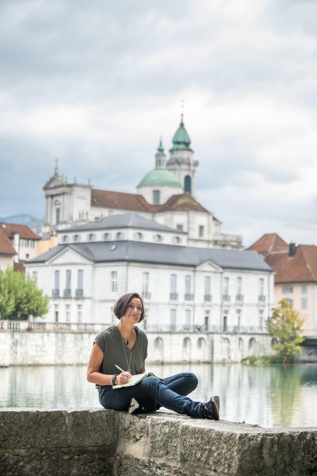 Anita Riner mit Notizbuch auf der Mauer an der Aare in Solothurn